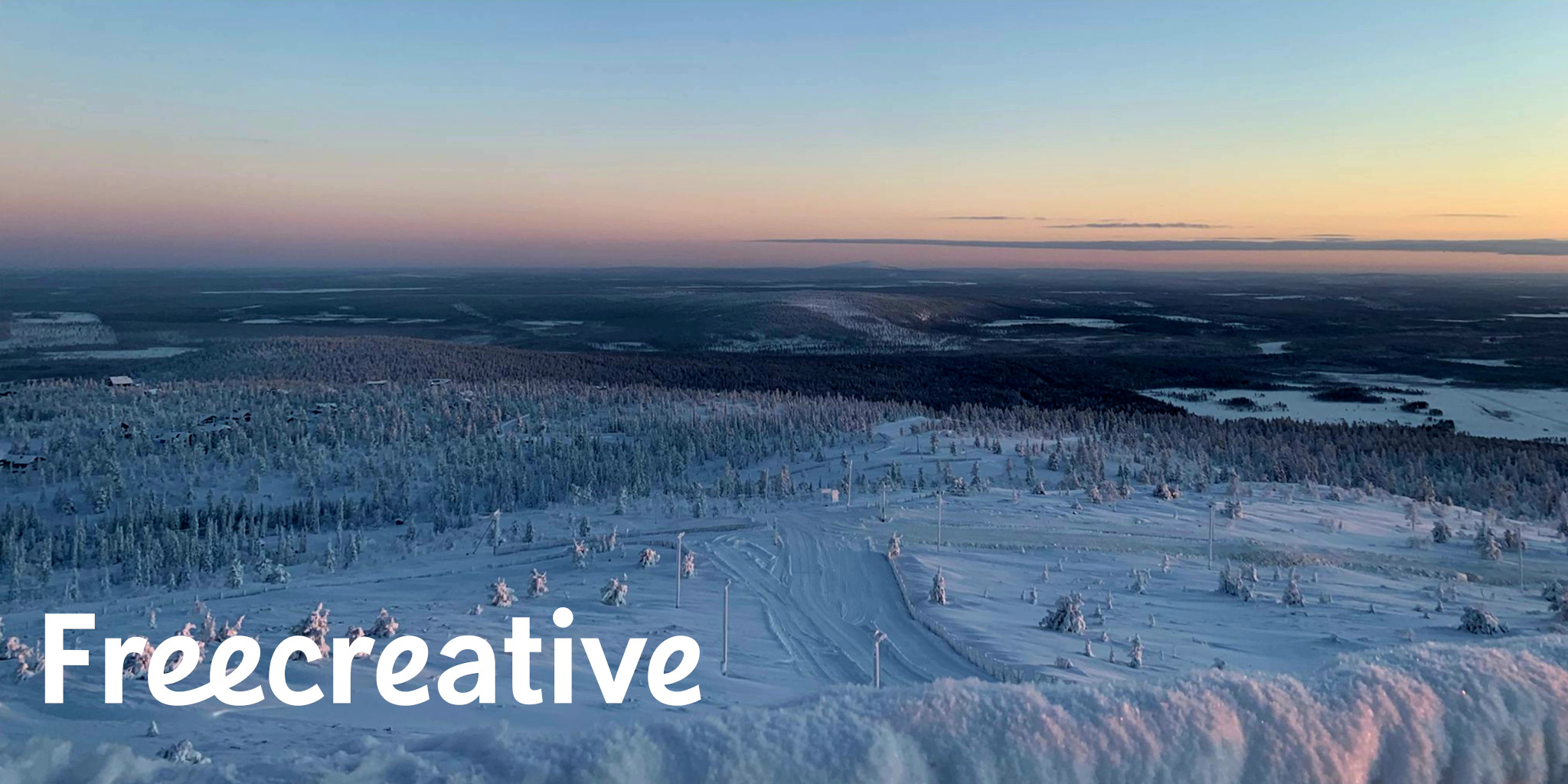 Luminen lappilainen maisema vaaran päältä talvella, vasemmassa alakulmassa Freecreativen logo