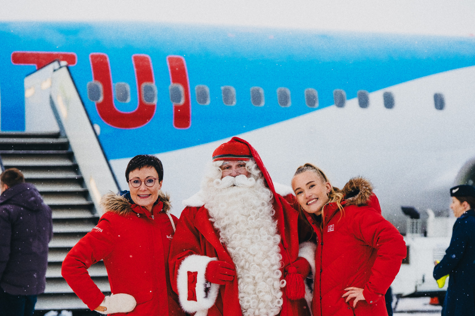 Visit Rovaniemen toimitusjohtaja Sanna Kärkkäinen poseeraa TUIn koneen edessä joulupukin ja apurin kanssa